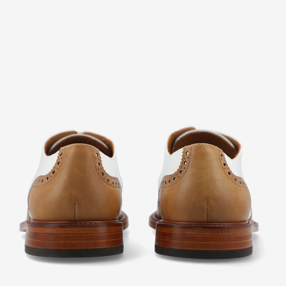 Rear view of a pair of brown and white dress shoes with brogue detailing, placed against a plain white background.