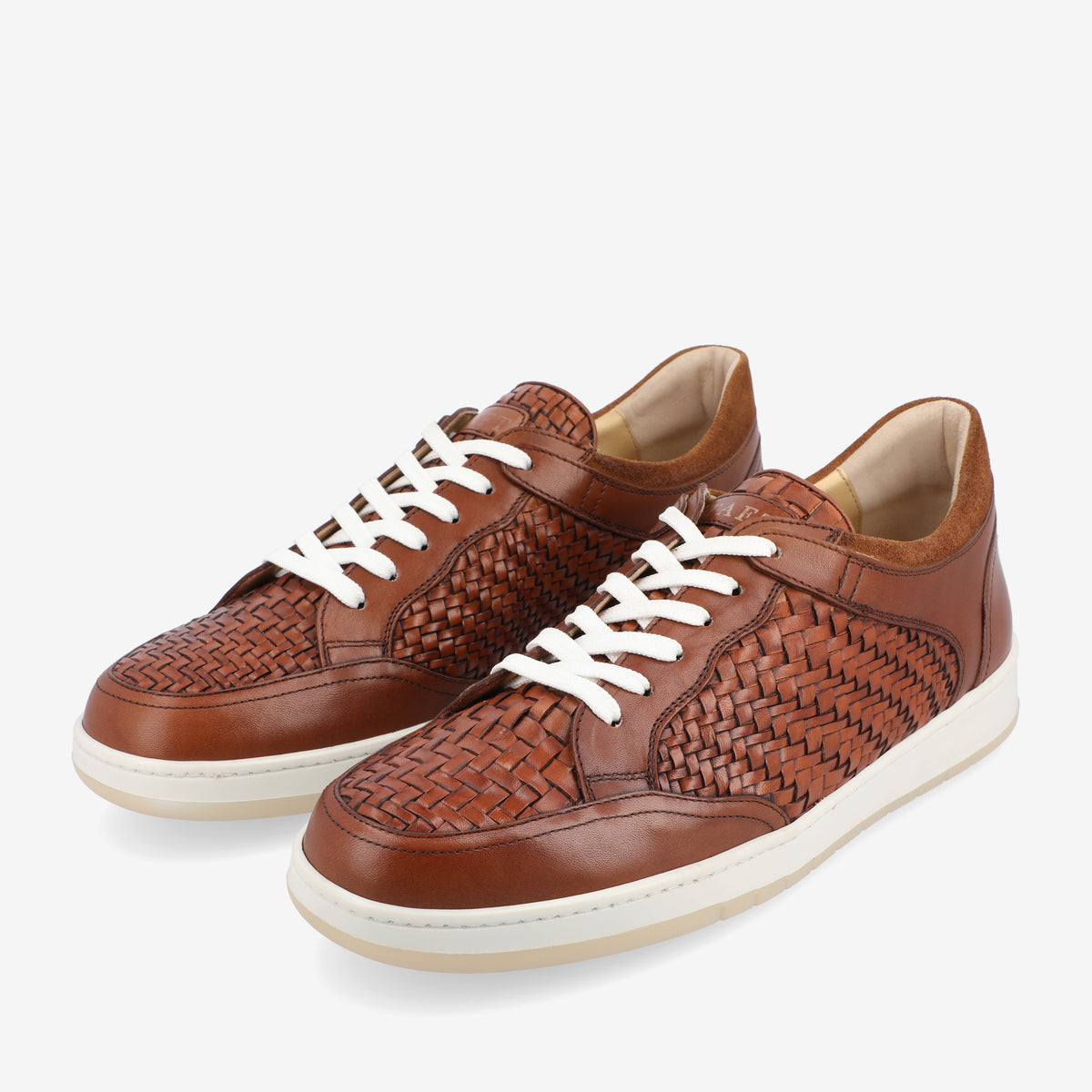 A pair of brown leather sneakers with white laces and woven detailing on the sides, set against a white background.