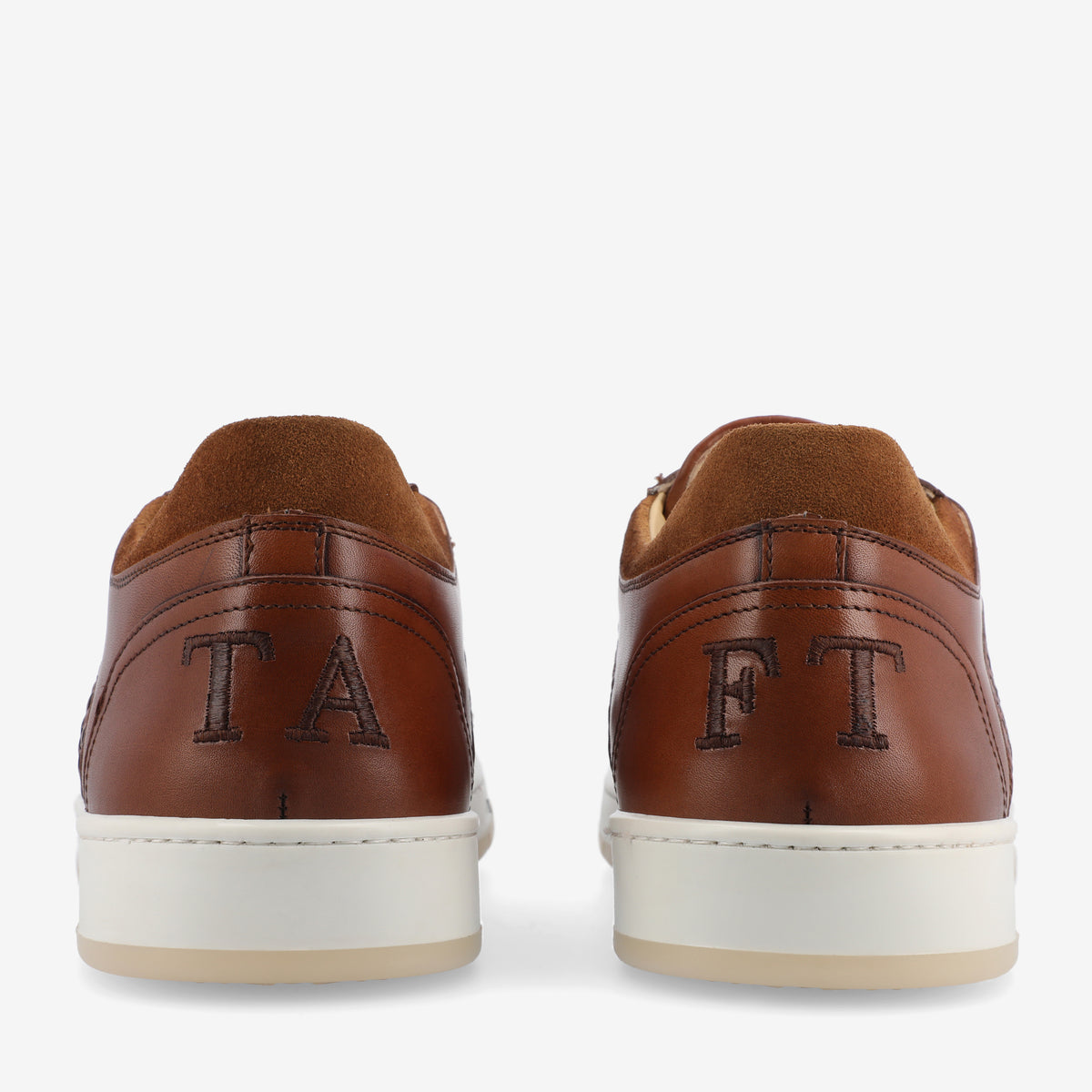 A pair of brown leather shoes with white soles, featuring the letters TA on the left shoe and FT on the right shoe.