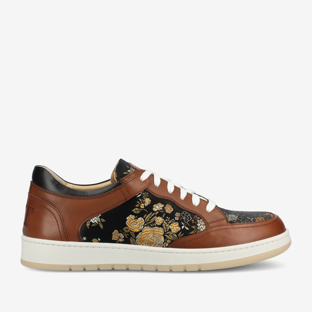 Side view of a brown leather sneaker with white soles and laces, featuring an intricate floral pattern on the black fabric side panels.