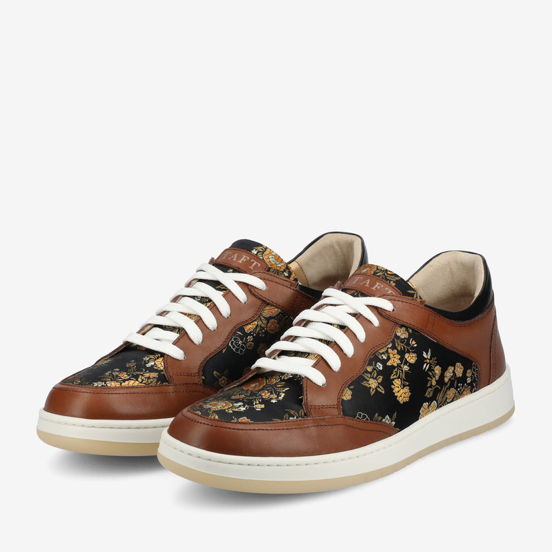 A pair of black and brown floral-patterned sneakers with white soles and white laces are displayed against a plain white background.