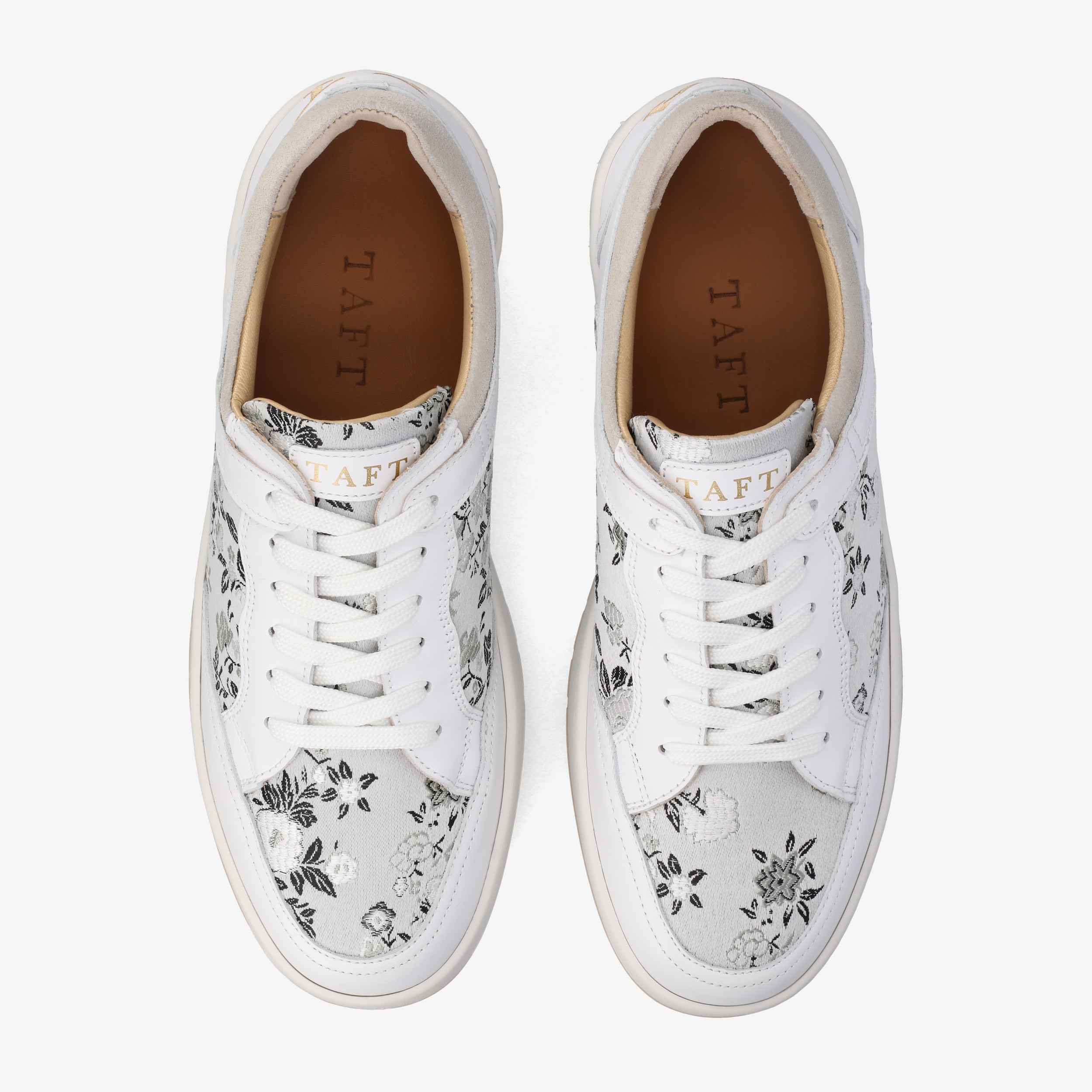 Pair of white sneakers with black floral patterns, white laces, and brown insoles marked TAFT.