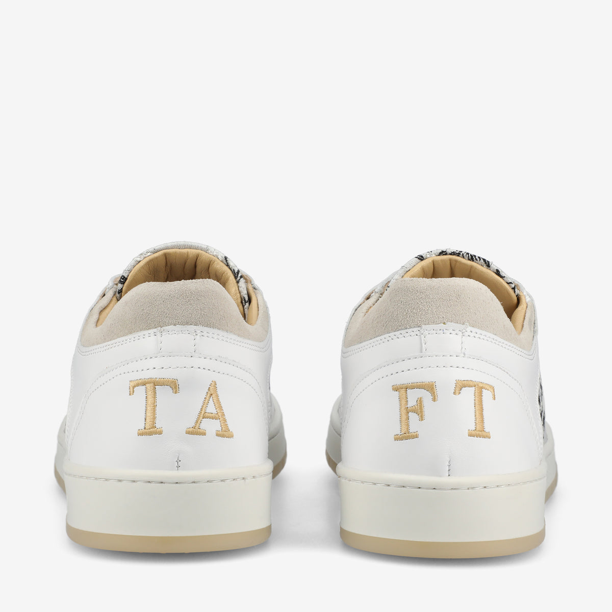 Rear view of a pair of white sneakers featuring the letters TA on the left shoe and FT on the right shoe. The shoes have beige accents on the heel and a white sole.