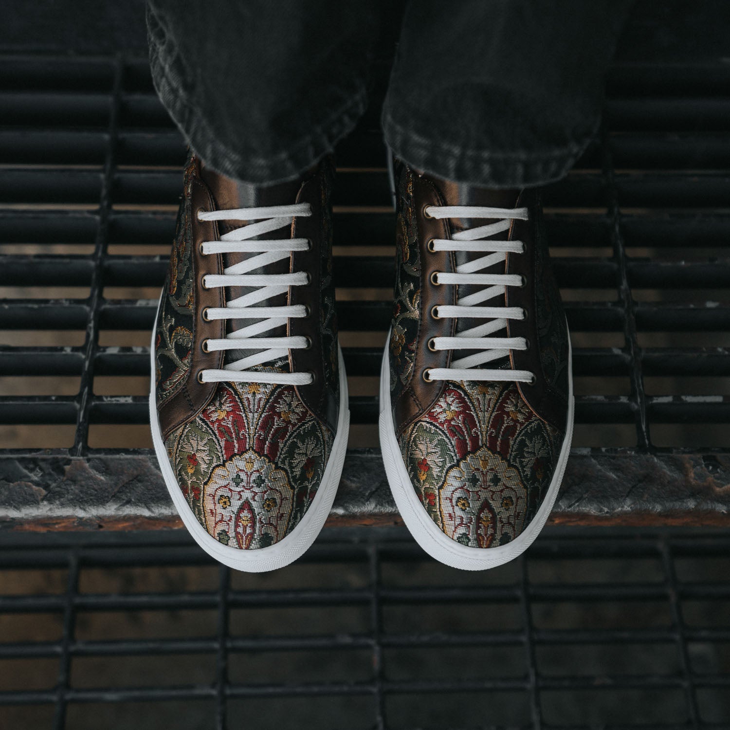 A close-up of feet wearing patterned sneakers with white laces, standing on a metal grate floor.