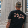 A person wearing a black T-shirt with the text Take Care of Yourself stands near a series of white columns.