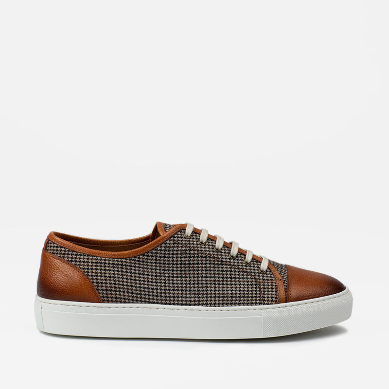 Side view of a low-top sneaker with a white sole, brown leather accents, and a houndstooth textile pattern on the sides and upper.