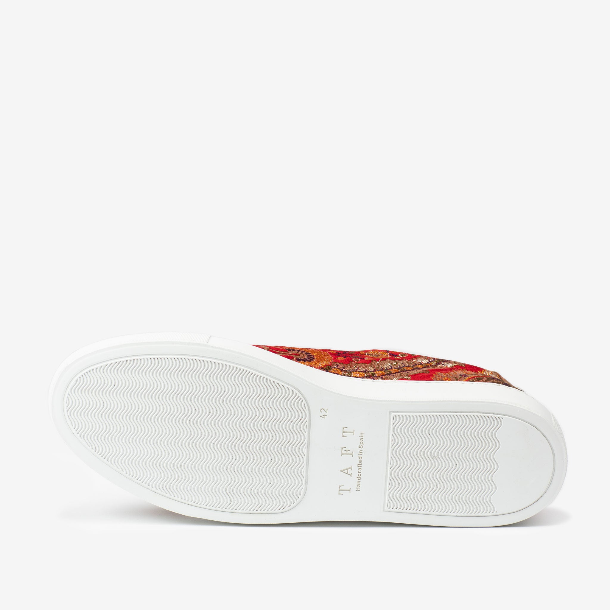 Bottom view of a sneaker with a white rubber sole, displaying the brand name TAFT. The upper part of the shoe features a colorful pattern with red and orange tones.