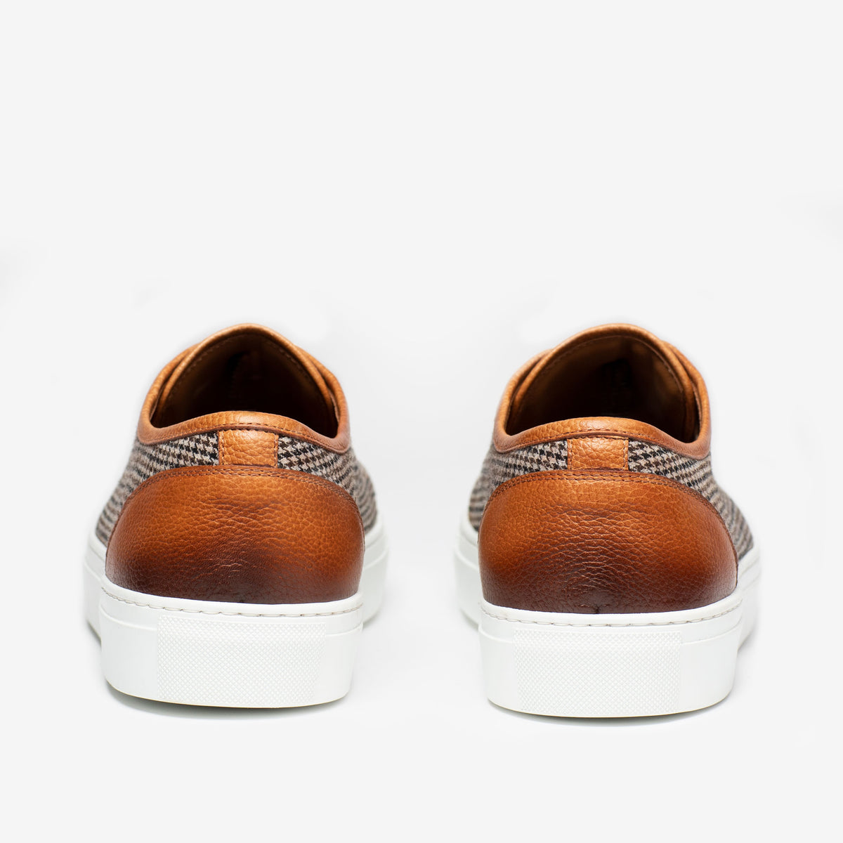 Rear view of a pair of brown leather sneakers with white soles on a plain white background.