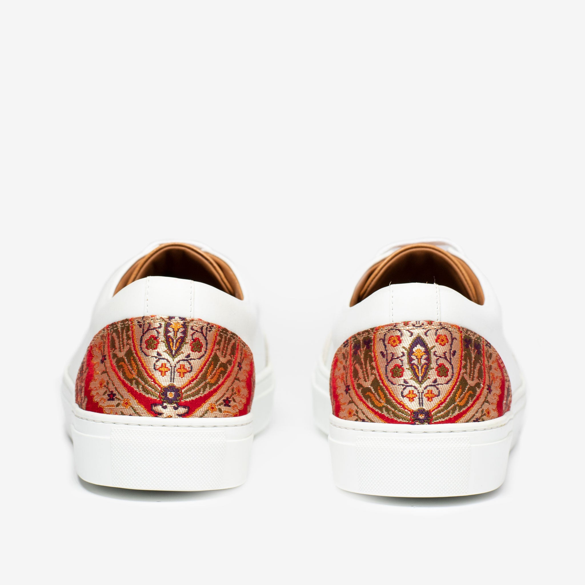 Back view of white sneakers with intricate red, orange, and green patterned detailing on the heels, against a plain white background.