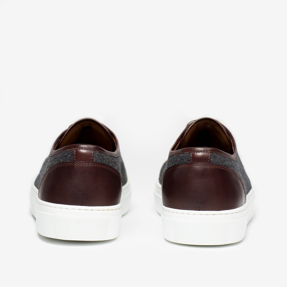 Rear view of a pair of casual shoes with dark brown leather uppers, gray fabric sections, and white rubber soles, set against a white background.