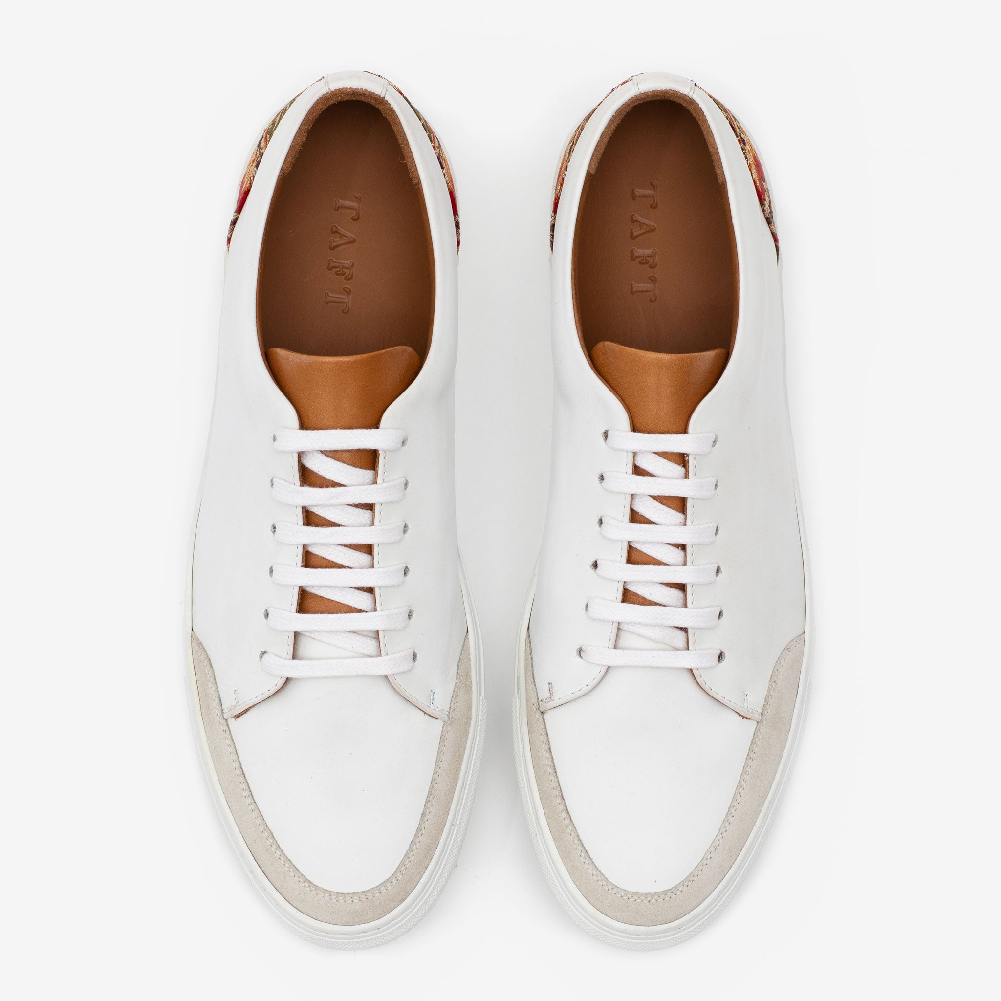 Top view of a pair of white lace-up sneakers with tan interiors and subtle beige accents on the toe and heel areas.