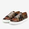 A pair of lace-up sneakers with brown leather accents and black fabric featuring a floral pattern with gold and bronze tones.