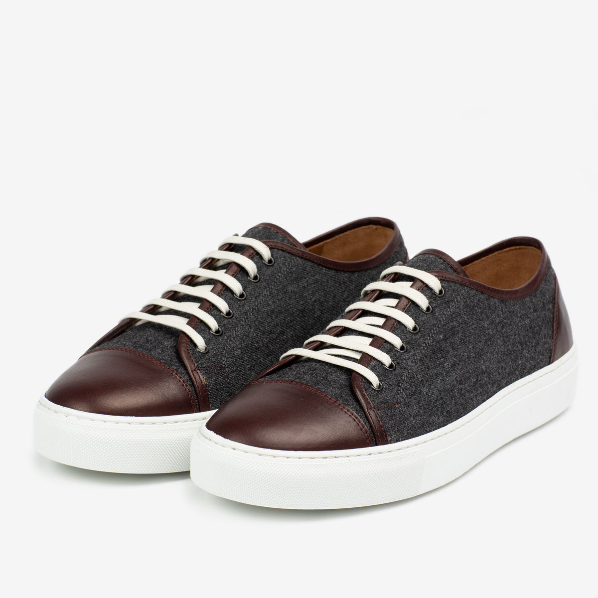 A pair of low-top sneakers with dark brown leather toe caps, gray fabric uppers, white laces, and white rubber soles.