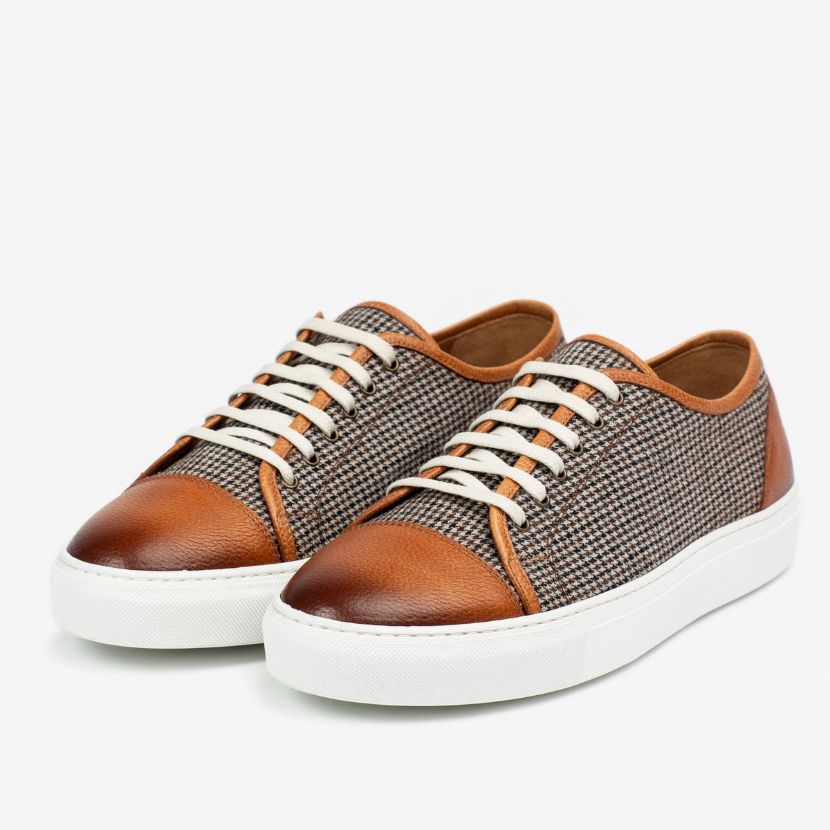 A pair of brown and white sneakers with brown leather accents and beige laces, featuring a houndstooth pattern on the sides, displayed on a white background.