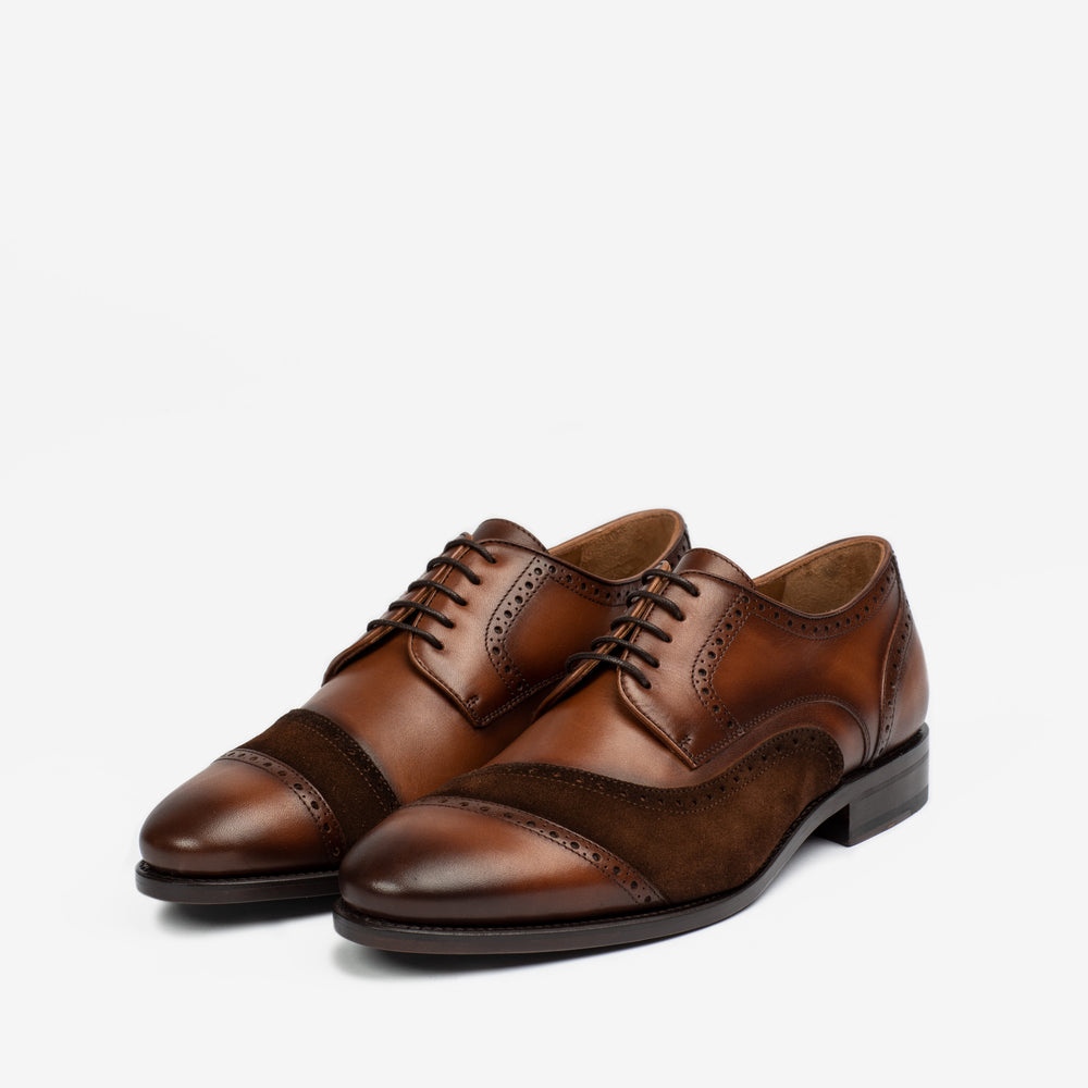 A pair of brown leather oxford shoes with punched detailing and contrasting suede panels, placed on a white background.