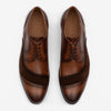 A pair of brown leather dress shoes with brogue detailing and dark brown suede accents viewed from above.