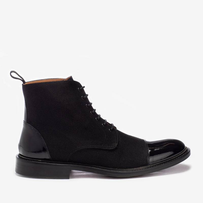 Black suede and patent leather lace-up boot with a pull tab at the back, leather sole, and a round-toed design, photographed on a plain white background.