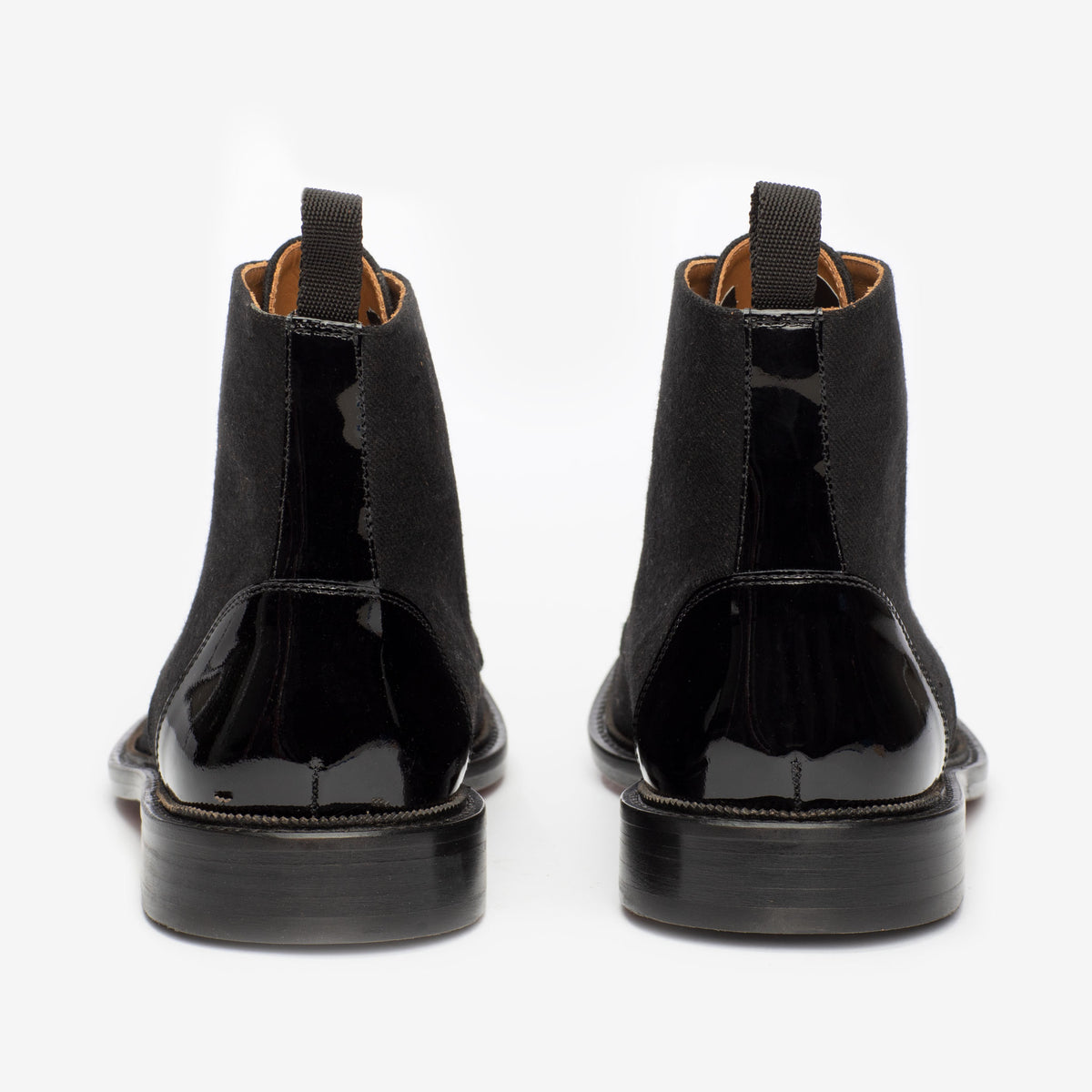 Rear view of a pair of black leather Chelsea boots with suede panels and elastic side panels, placed side by side against a white background.