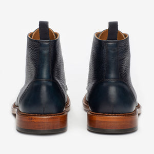 A pair of dark blue leather ankle boots with brown soles viewed from the back.