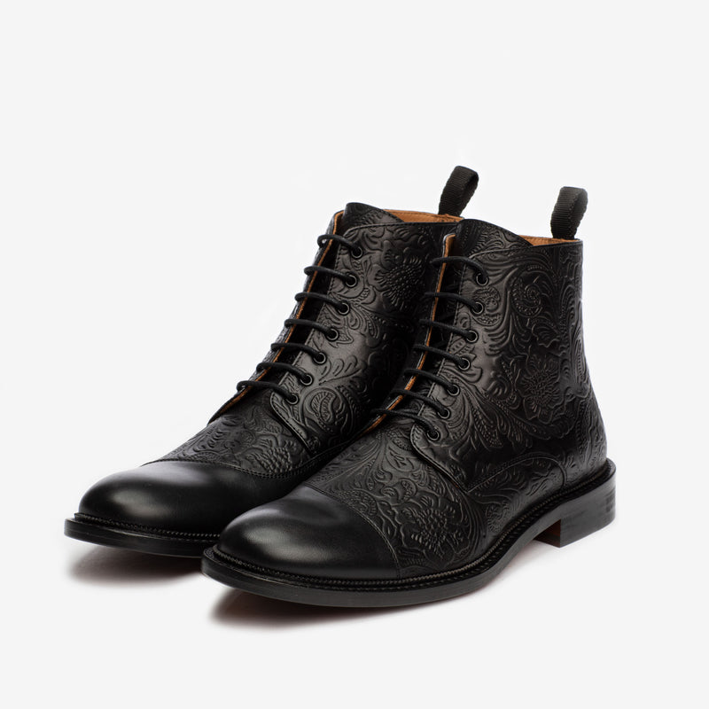 A pair of black leather ankle boots with intricate embossed patterns, laces, and pull tabs on a white background.