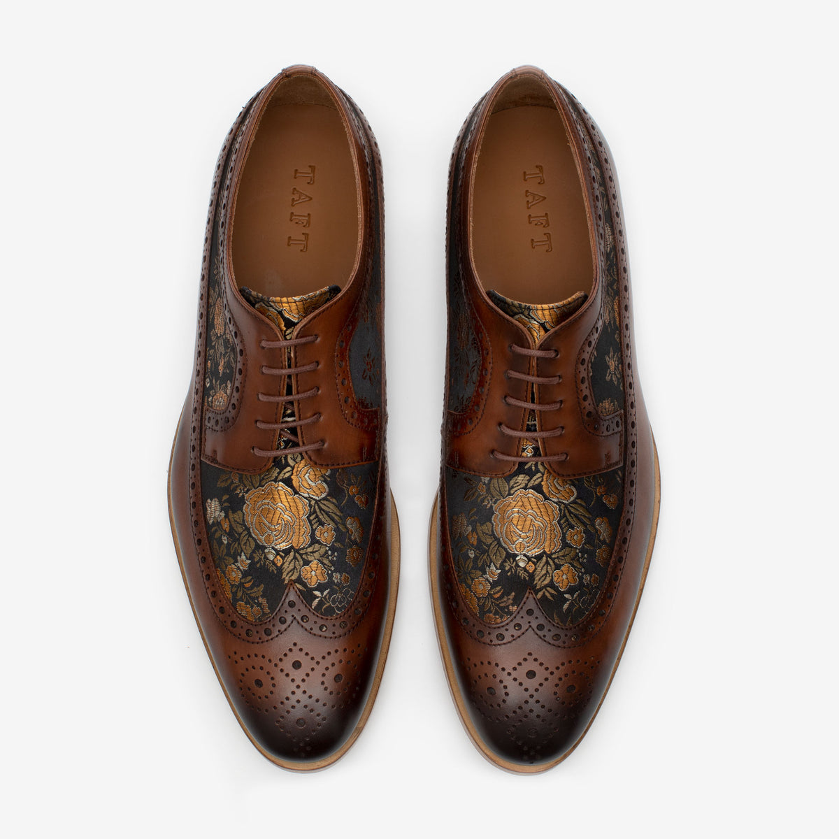 A pair of brown leather dress shoes with decorative floral patterns and brogue detailing, shown from above.