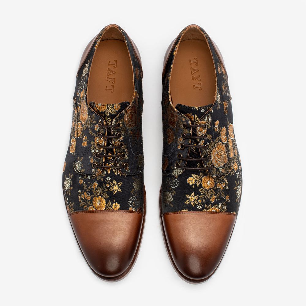 A pair of dress shoes with a floral pattern on the upper and brown leather cap toes, featuring laces and leather insoles labeled TAFT.