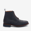 A side view of a dark blue leather ankle boot with a cap toe design, brown laces, and a pull tab at the heel. The boot has a sturdy sole with visible treads.