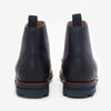 Back view of a pair of navy blue leather ankle boots with pull tabs and rubber soles, displayed on a white background.