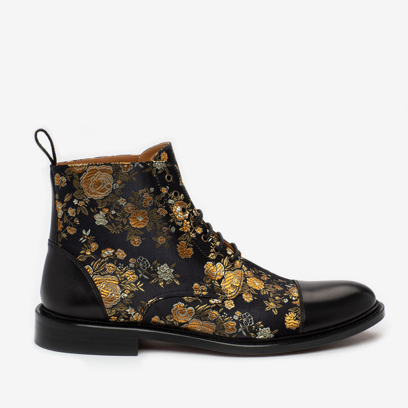 Black leather boot with intricate golden floral embroidery, featuring a lace-up front and a pull tab at the heel.