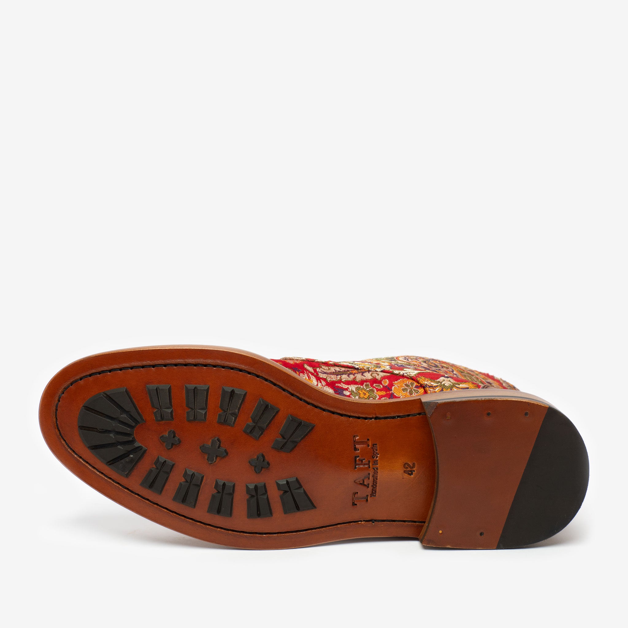 The image shows the sole of a patterned dress shoe, featuring a red and gold fabric upper and a brown rubber sole with black traction patterns. The brand name TAFT is imprinted on the sole.