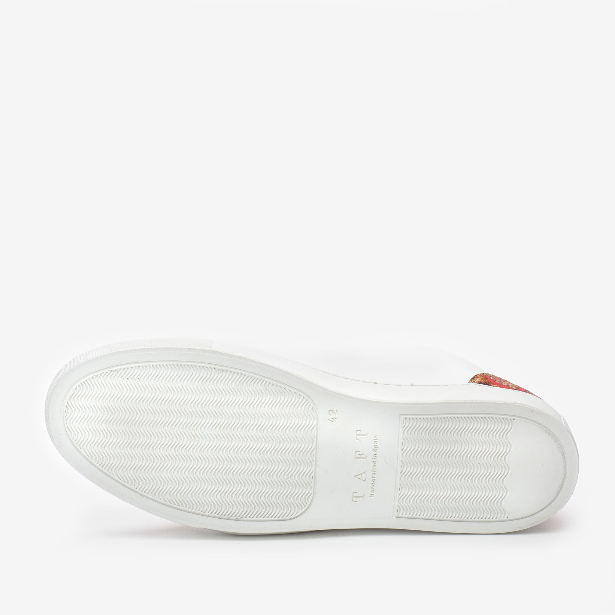 The image shows the bottom view of a white sneaker with a textured sole and the text TAFT written on it.