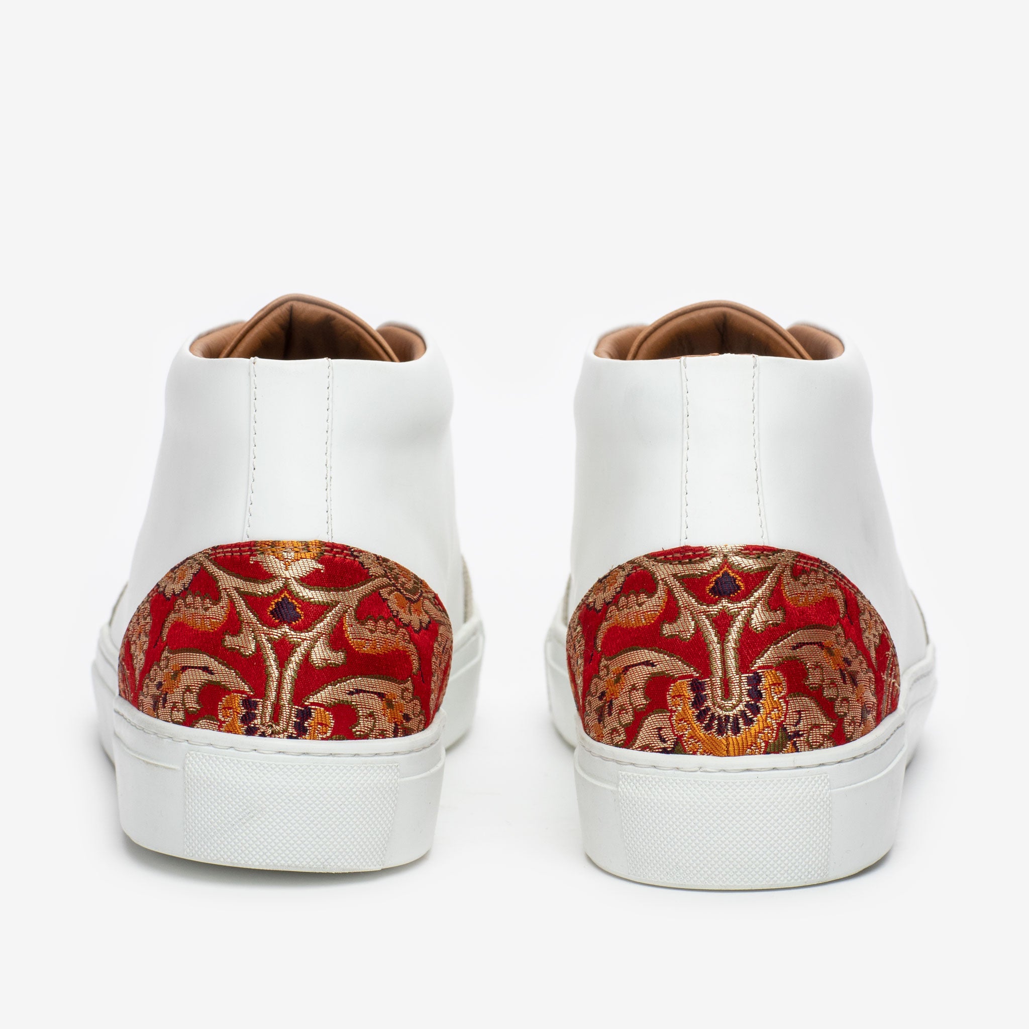 A close-up of the back of a pair of white sneakers with decorative red and gold embroidered detailing on the heels.