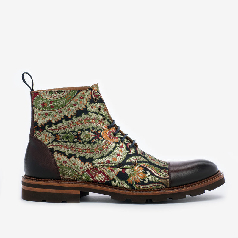 A single, patterned boot with a combination of green, red, and black floral designs, leather accents, and a brown sole with laces.