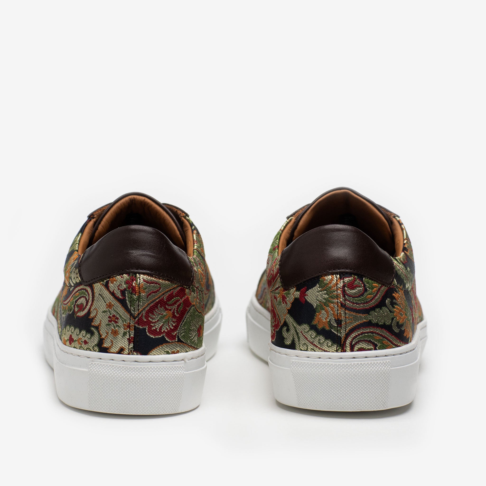 Back view of a pair of low-top sneakers featuring a colorful paisley pattern with dark brown leather accents and white soles.