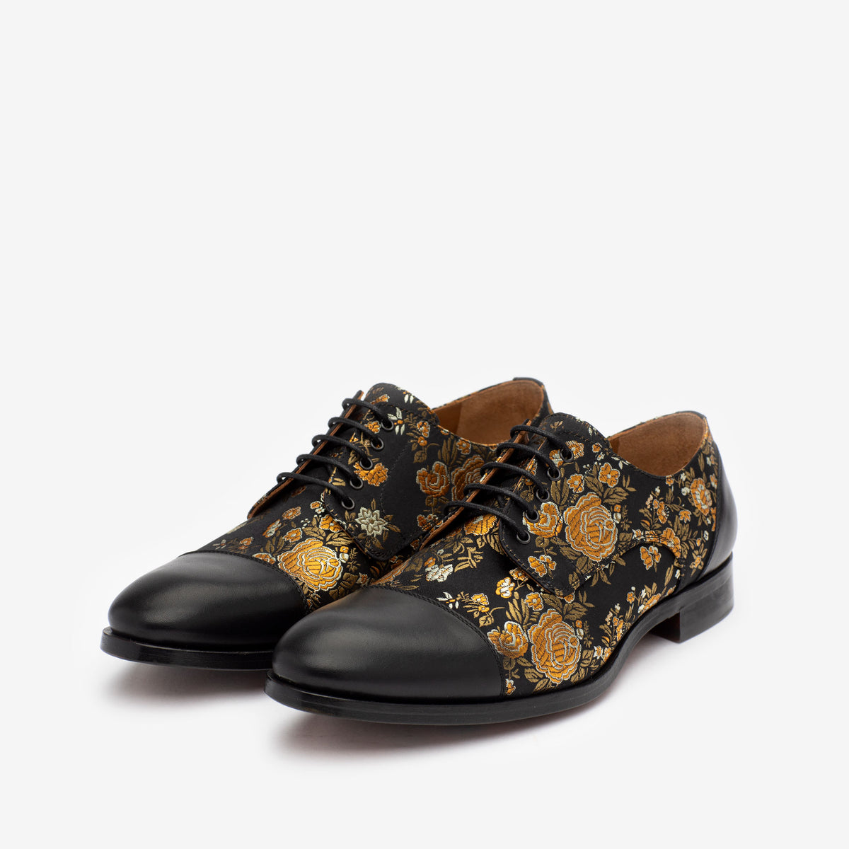 A pair of black leather dress shoes with intricate gold floral designs and black laces.