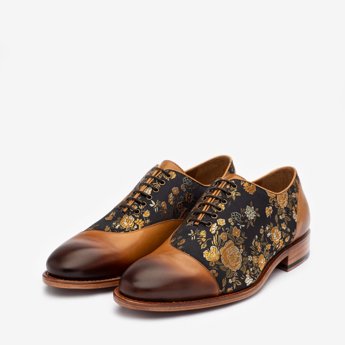 Pair of men's dress shoes featuring a combination of brown leather and black fabric with a floral pattern, set against a plain white background.