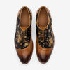 A pair of brown leather Oxford shoes with a floral-patterned fabric inlay, featuring intricate gold and black designs.