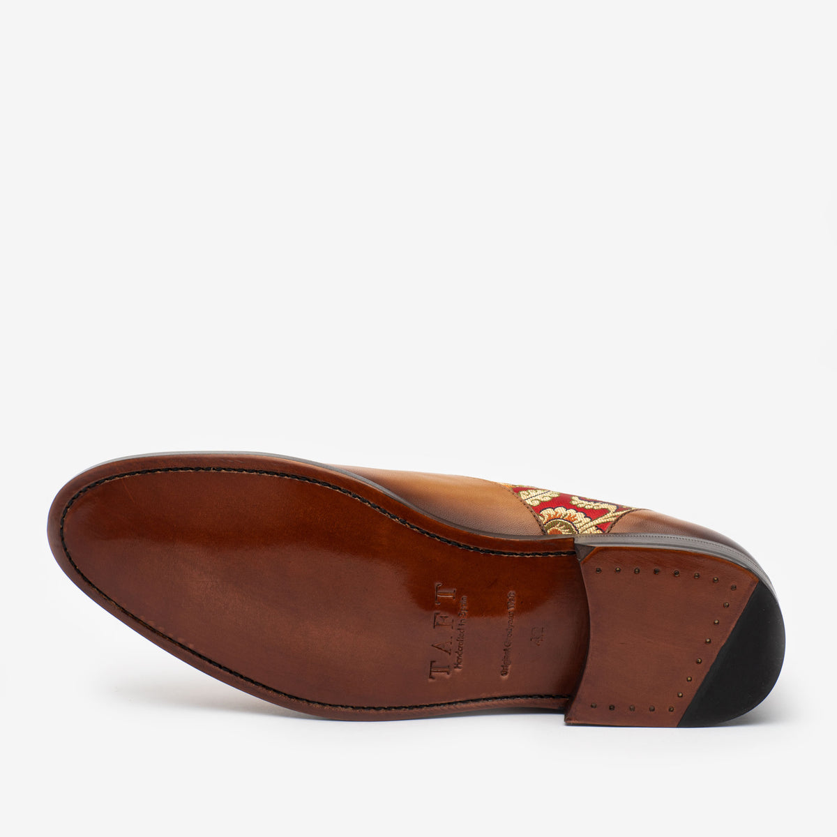 Bottom view of a brown leather dress shoe with a stitched sole, featuring patterned embroidery on the side and metal stud details on the heel.