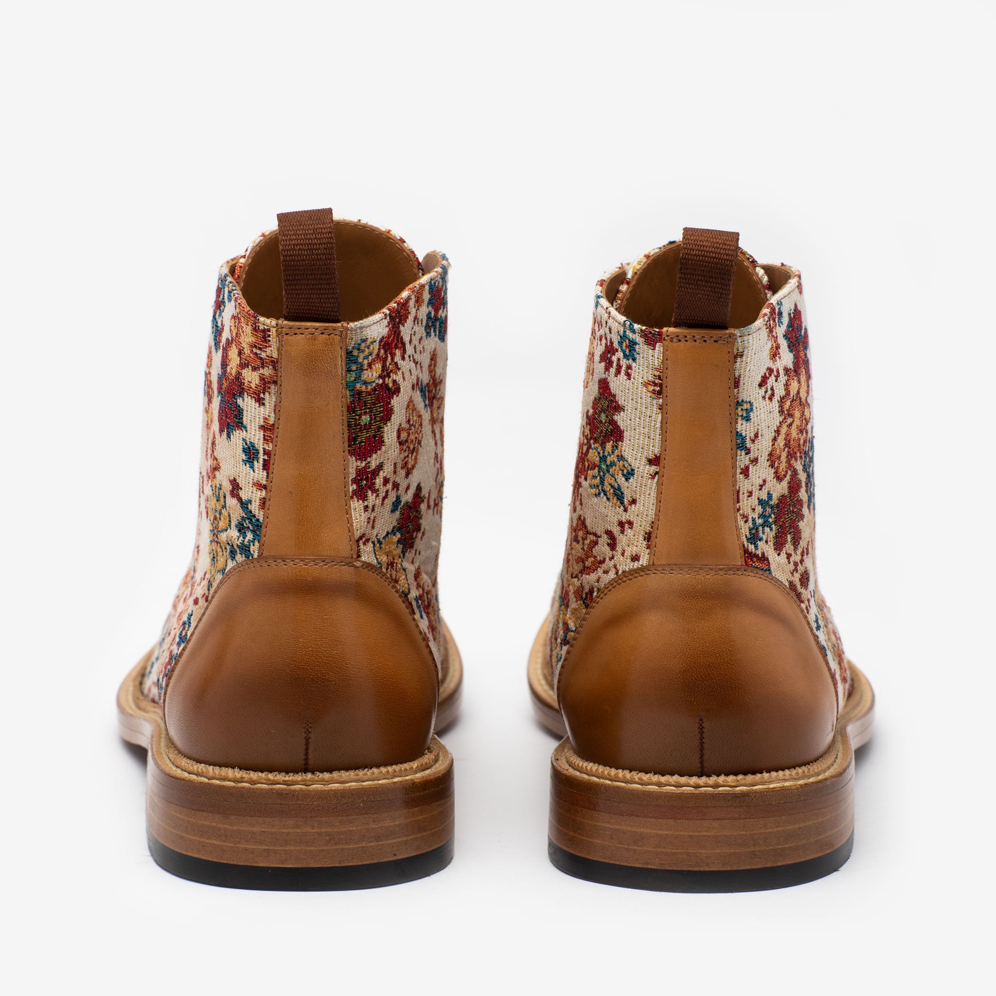 A pair of boots with a tan leather base and floral-patterned fabric uppers, displayed from the back against a white background.