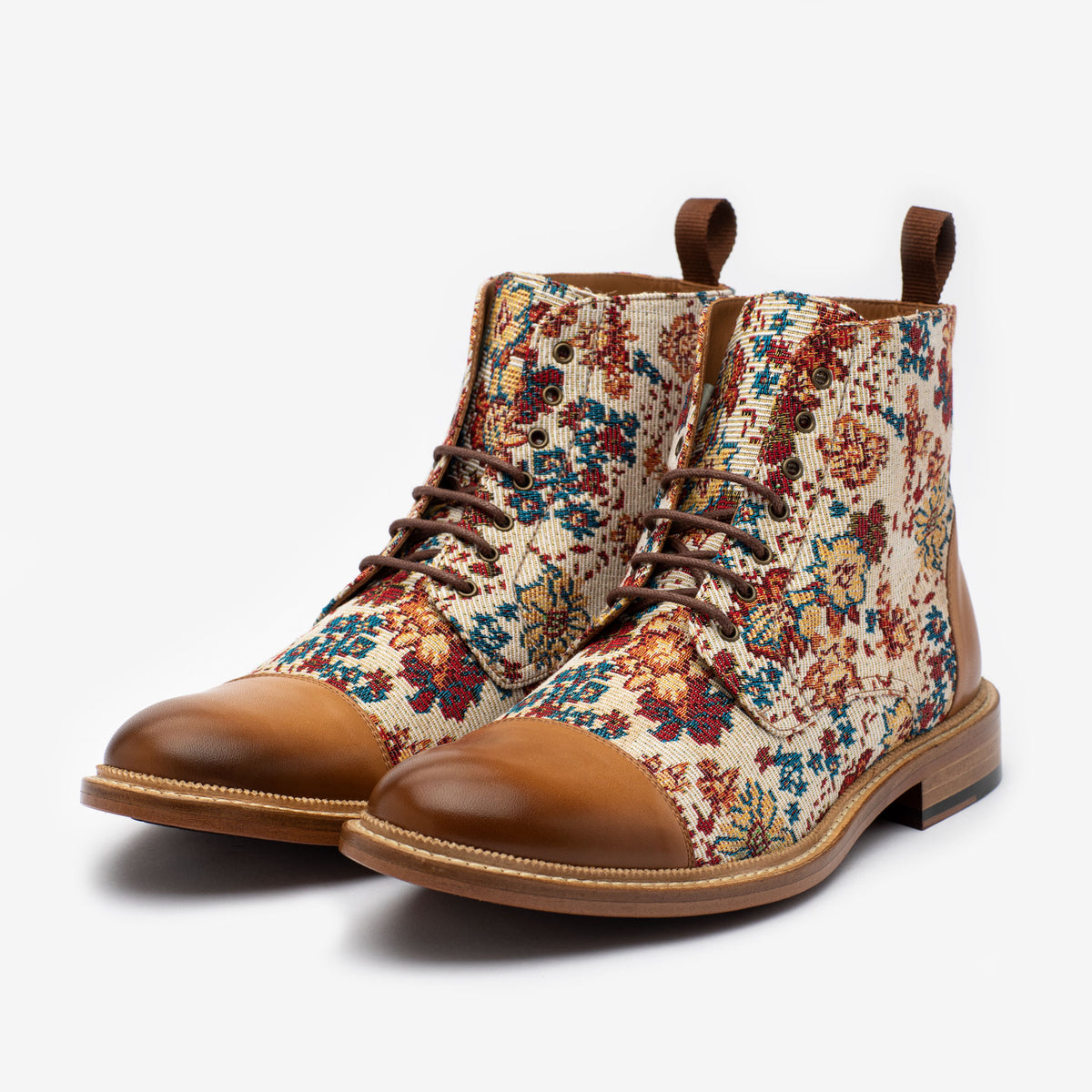 A pair of ankle-high boots with brown leather toe caps and heels, featuring a colorful floral tapestry fabric on the sides.