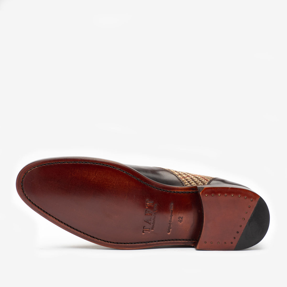 The sole of a dress shoe, showcasing a polished brown leather underside with the brand name, size, and model engraved. The shoe features a black leather and woven upper.