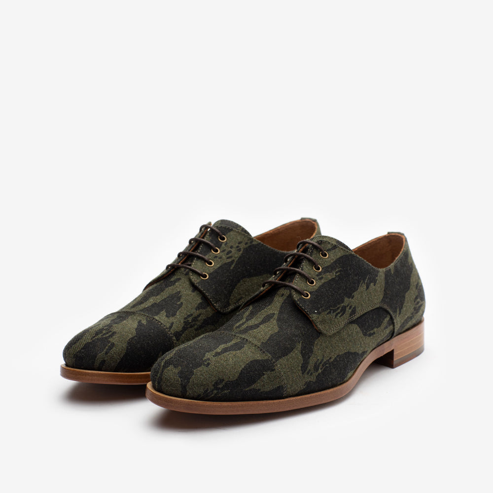 A pair of green camouflage pattern lace-up dress shoes with light brown soles on a plain white background.