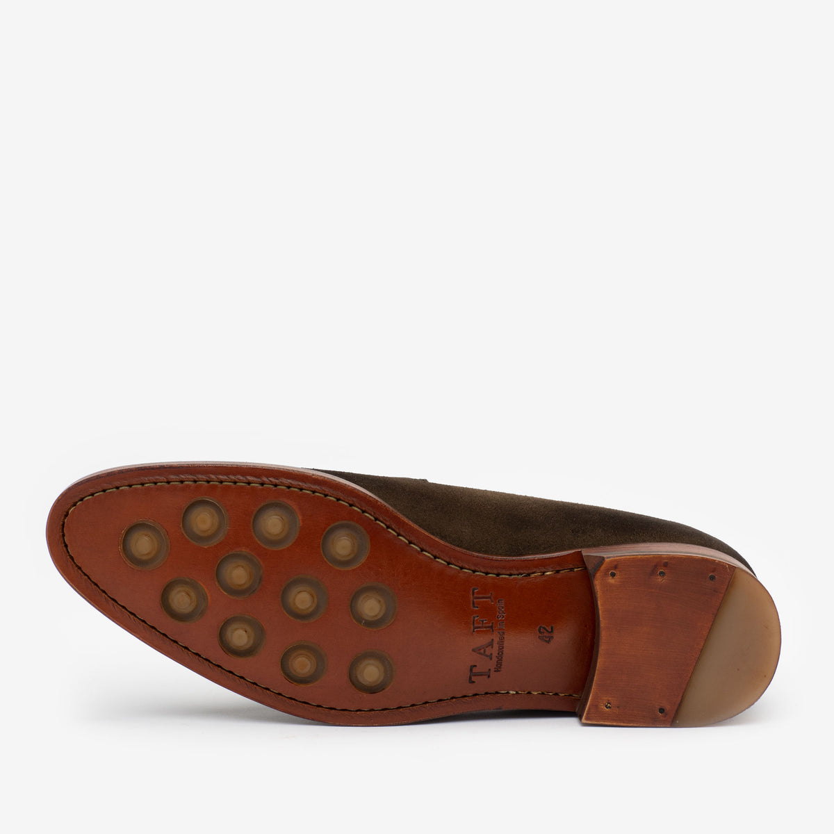 The image shows the bottom view of a brown leather shoe featuring a smooth sole with circular rubber grips and the brand TAFT imprinted on it.