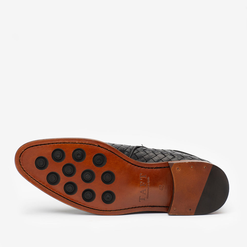 A bottom view of a black dress shoe showing a brown leather sole with black rubber grips and TAFT branding.