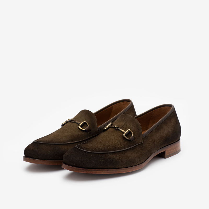 A pair of brown suede loafers with gold horsebit detailing on a white background.