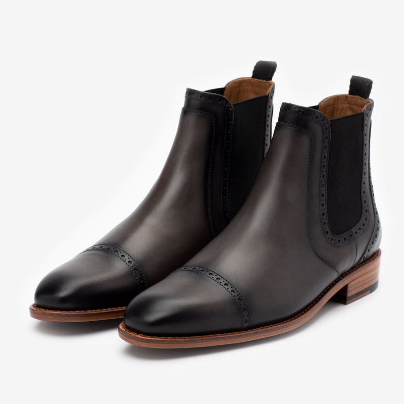 A pair of black leather Chelsea boots with brogue detailing and a wooden sole.