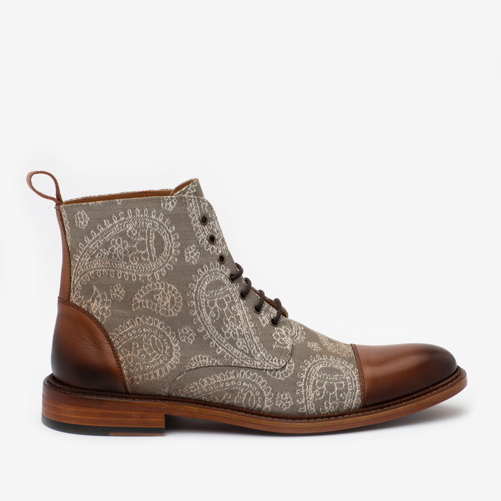 A single boot featuring a paisley-patterned fabric upper with brown leather trim and toe, a lace-up front, and a wooden sole.