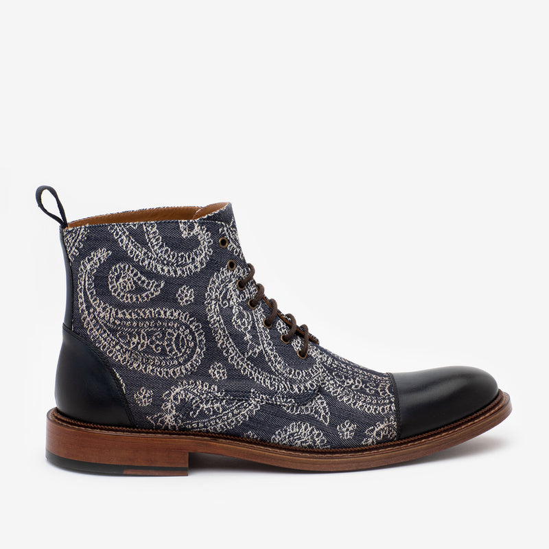 A blue paisley-patterned ankle boot with black leather toecap, laces, and a brown sole.