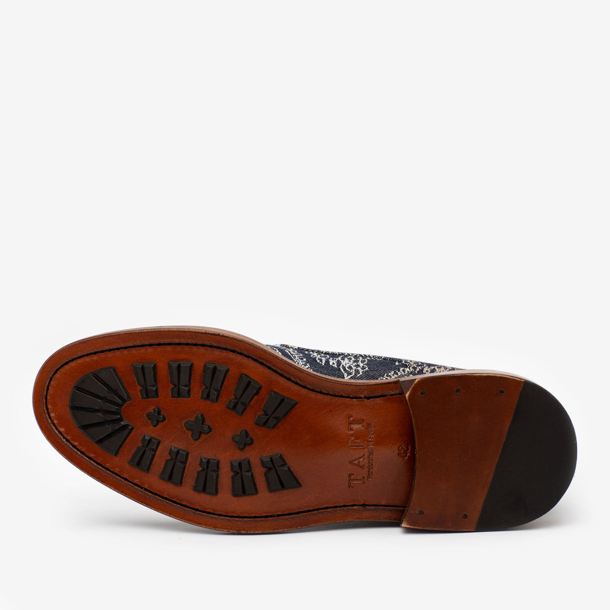 A single shoe is shown from underneath, featuring a brown sole with black, textured traction patterns. The brand name TAFT is imprinted on the sole.