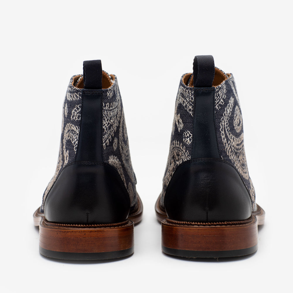 Pair of ankle-high leather shoes with intricate paisley patterns on the fabric, wooden soles, and black pull tabs, viewed from the back.